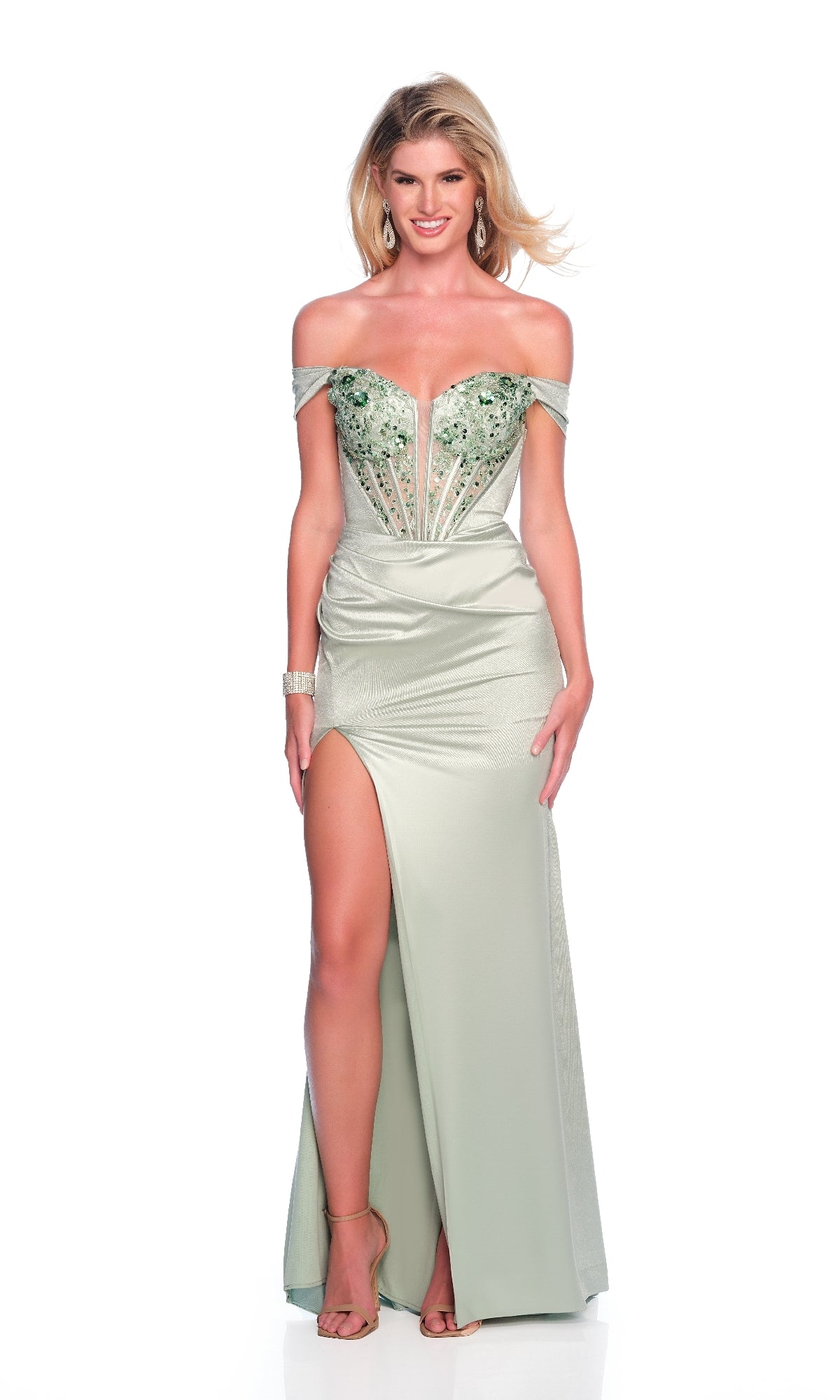 A woman wearing the Long Prom Dress: Dave and Johnny 12186 in sage green, featuring a corset bodice, off-the-shoulder neckline, thigh-high slit, embellished details, and strappy heels stands against a white background.